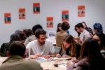 A group of people enjoying a coloring activity with bright orange posters in the background. A group of people enjoying a coloring activity with bright orange posters in the background.