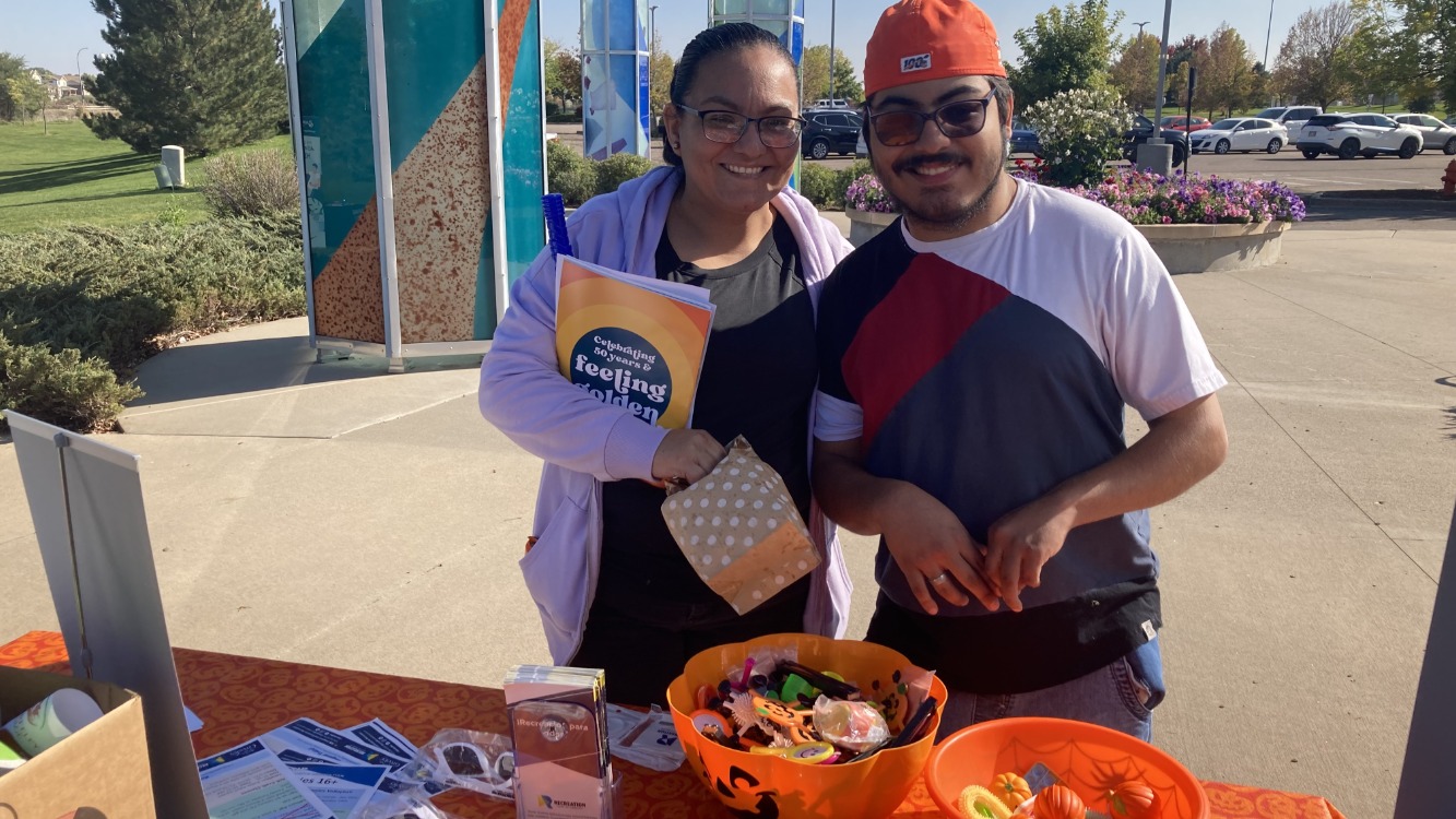 A man and woman stand by a booth with resources and a bowl of Halloween candy at the Family FunPlex