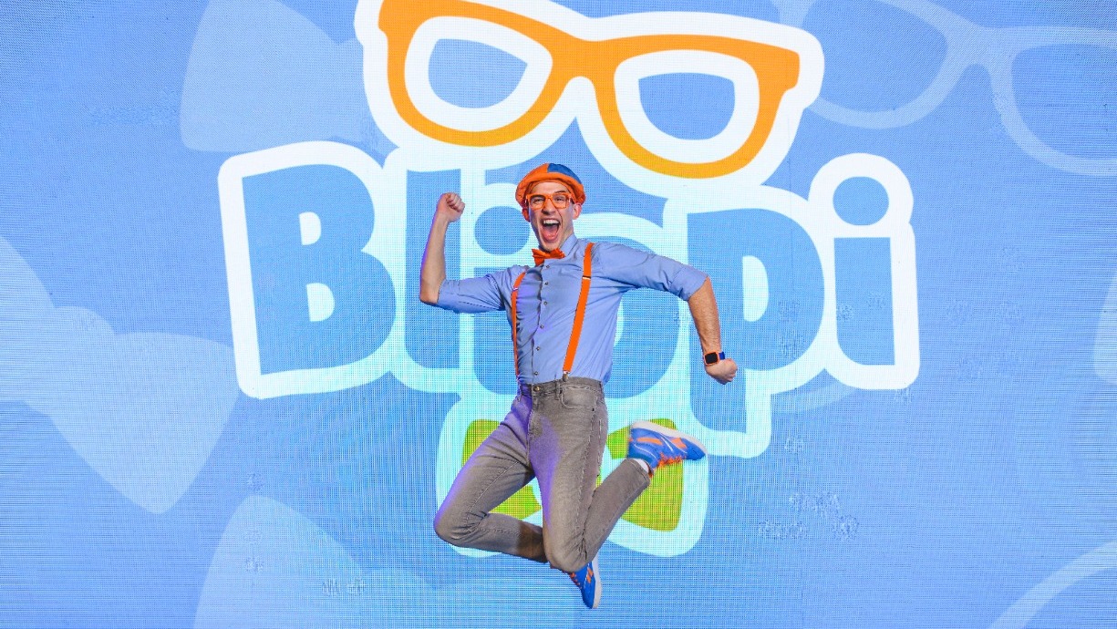 Man wearing suspenders and jeans jumping in air in front of word "Blippi"