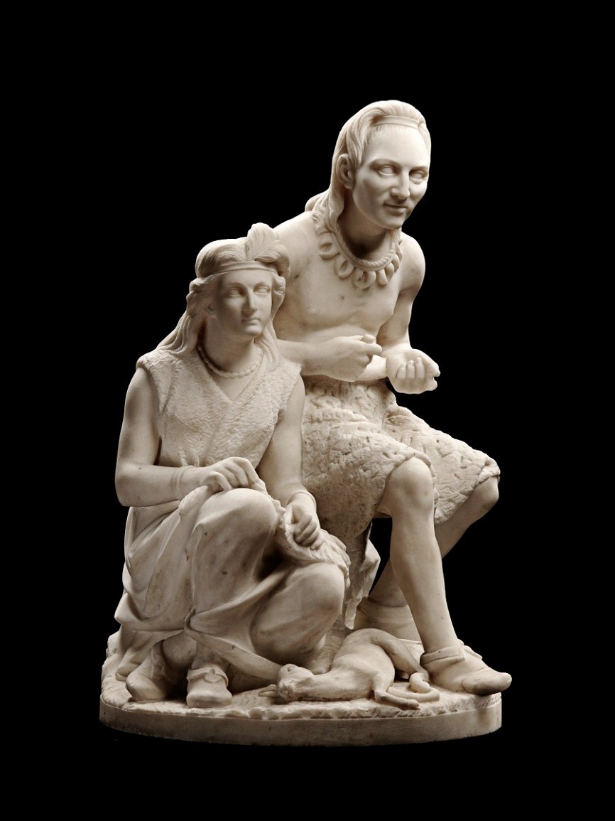 A marble sculpture of two figures; one is sitting on the ground, the other is sitting on a stool. 