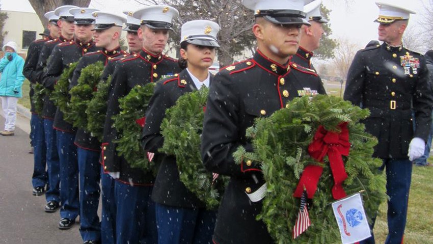 Men and women in US veteran uniforms stand in a single file line holding wreaths at the annual Wreaths Across America Ceremony 