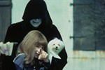 The grim reaper holds a tiny white dog and smiles down upon young Valerie who points at the camera