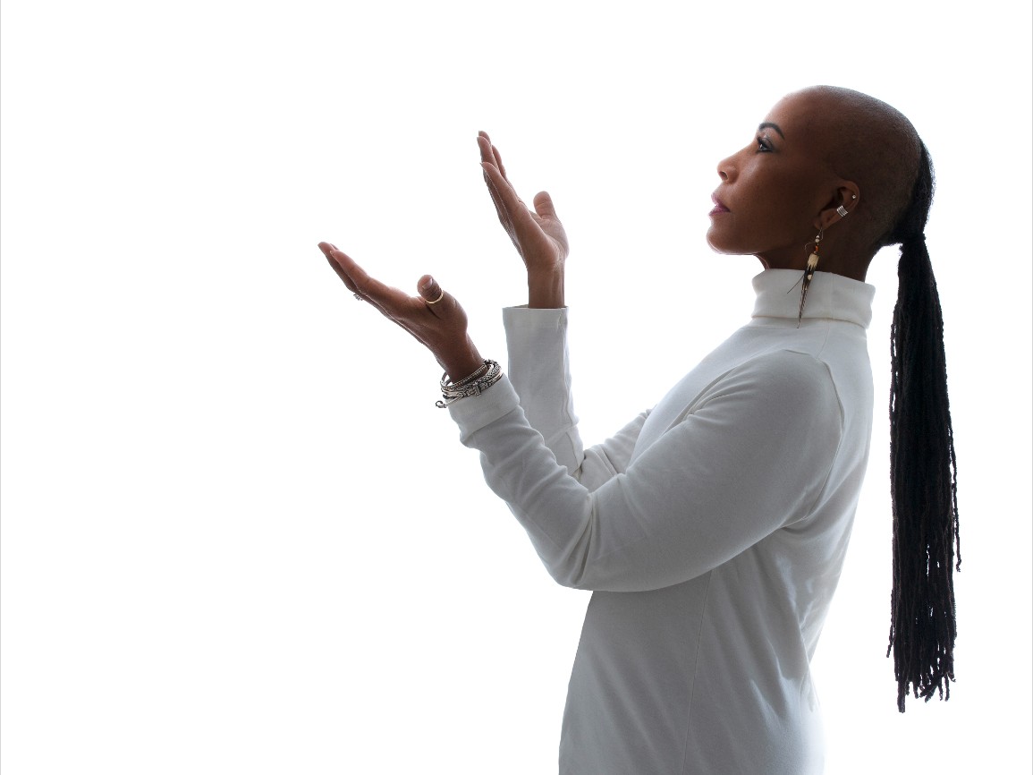 Photographic profile portrait of an African American woman with long straight hair. The woman is wearing a white turtleneck.