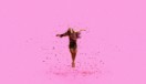 A woman against a bright pink background, jumping into the air with confetti all around.