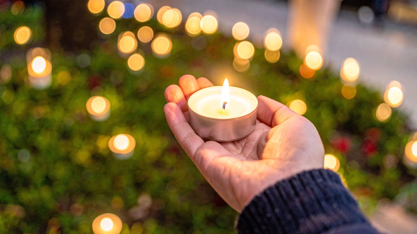 A hand holding a candle with candle lights glowing in the background