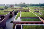 Aerial view of a low-rise brick complex with grass-covered roofs arranged in a maze-like pattern, set within a rural landscape of fields and trees.