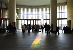 A crowd of people in silhouetted against a wall of windows with a rainbow cast on of floor in the foreground A crowd of people in silhouetted against a wall of windows with a rainbow cast on of floor in the foreground