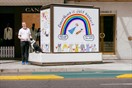 A man in a white shirt and black pants standing on the street, with a black and white dog, in front of a public artwork that has the writing 'everything is just perfect'.