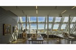 A sunlit museum classroom installed with few works of art has a wall of angled windows with a majestic view onto the horizon.