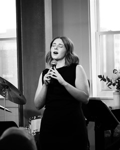 Black and white image of a woman singing into a microphone.