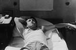 black and white image of a young white man lying in bed smoking