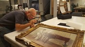A conservator uses a brush to clean a gold frame