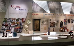 Museum cases titled "Giving in America", featuring a collection of objects related to philanthropy.