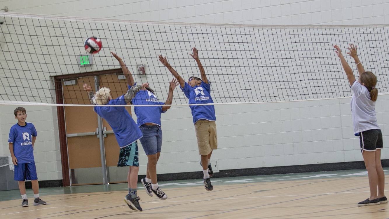 Boys and girls play volleyball in the gym.