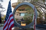 The flag of the United States and an eagle feather staff in front of the National Native American Veterans Memorial with the ceremonial flame lit on the grounds of the National Museum of the American Indian in Washington, DC, the museum's curved yellow stone building in the background The flag of the United States and an eagle feather staff in front of the National Native American Veterans Memorial with the ceremonial flame lit on the grounds of the National Museum of the American Indian in Washington, DC, the museum's curved yellow stone building in the background
