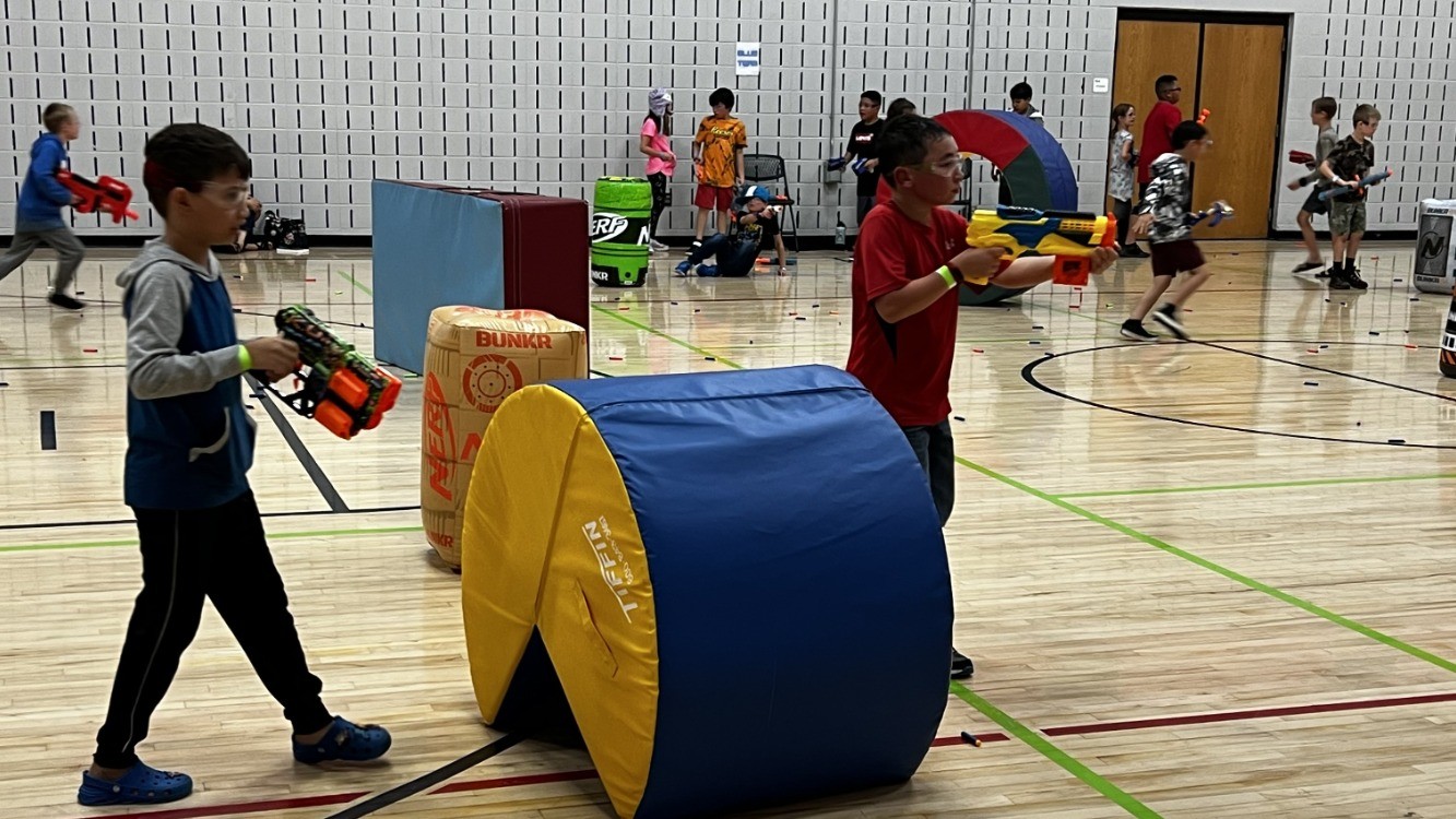 Boys and girls hide engage in NERF Wars in the gym