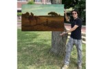 In this photomontage, a smiling young man stands next to a tree, gesturing toward a landscape painting that appears to float. In the foreground of the painting, two boys and a horse clear a large brown field.