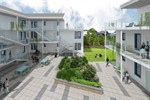 Modern apartment courtyard with people walking and sitting near raised green planters and outdoor seating, surrounded by white multi-story buildings.