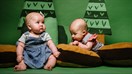 Two babies resting on cushions in front of a woodland set