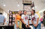 Three students smile in front of tri-fold poster board displays about Hawaiian language and history Three students smile in front of tri-fold poster board displays about Hawaiian language and history
