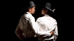 A couple in silhouette dressed in white shirts and black cowboy hats embrace each other around the waist A couple in silhouette dressed in white shirts and black cowboy hats embrace each other around the waist