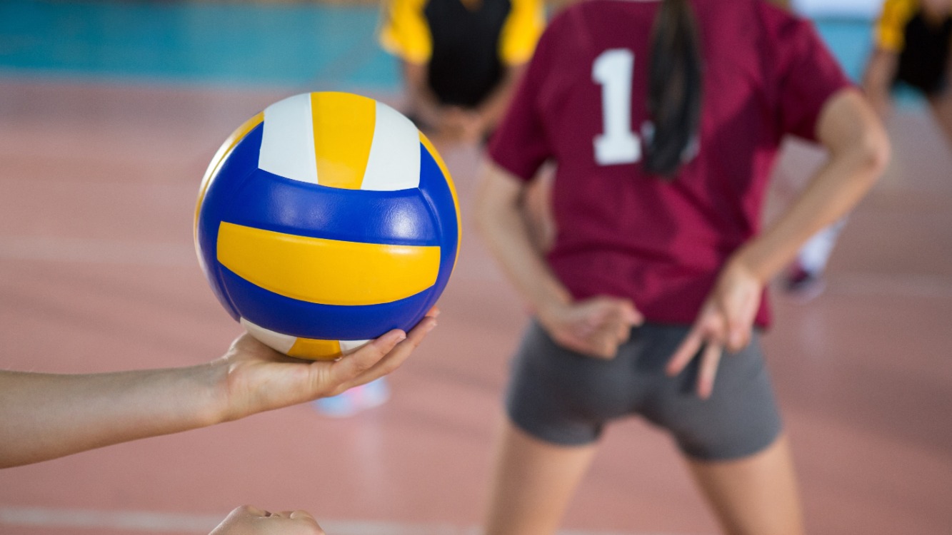 Women's volleyball game in the gym as one gets ready to serve.