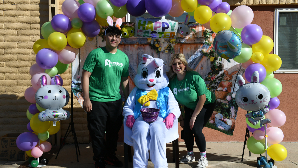 Two Greeley Recreation staff pose with the Easter Bunny at the photo booth with balloon arch during the annual Easter Egg Hunt at Rodarte Community Center.