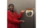 In this photomontage, a smiling young woman gestures toward a jug that appears to float. Printed in black on the jug’s surface is a Black man gesturing toward his chained wrist and the words “AM NOT I A MAN AND A BROTHER.”