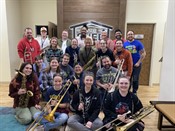 A large, diverse group of people hold musical instruments and smile for a photo.