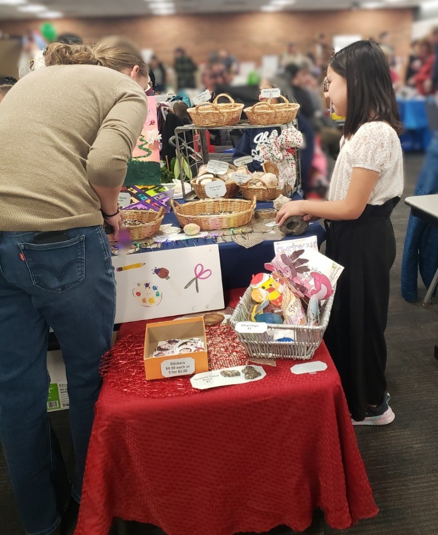 Child helping a customer at her vendor booth at the Kids Market Fair