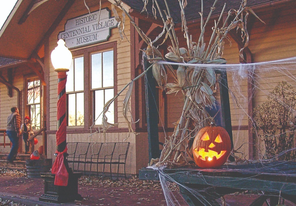 jack o lantern, cornstalks and spider webs decorate the outside of an old train depot building