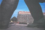 A building under construction seen in the distance through the legs of a statue