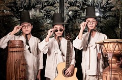 Three men wearing white clothes, traditional Korean hats, and round glasses look into camera. Each stand with an instrument.