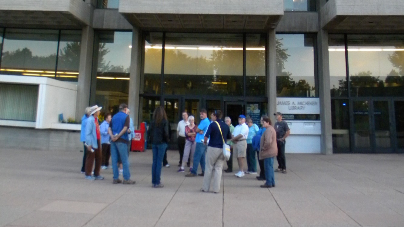 A group of people stand outside the entrance of Michener Library.