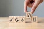 Blocks with DNA, apple, heart, longevity, and people exercising, with hand picking up longevity block.