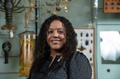 Jessica Ware, a female scientist with medium-brown skin and long dark hair, stands in a room surrounded by invertebrate specimens and artwork
