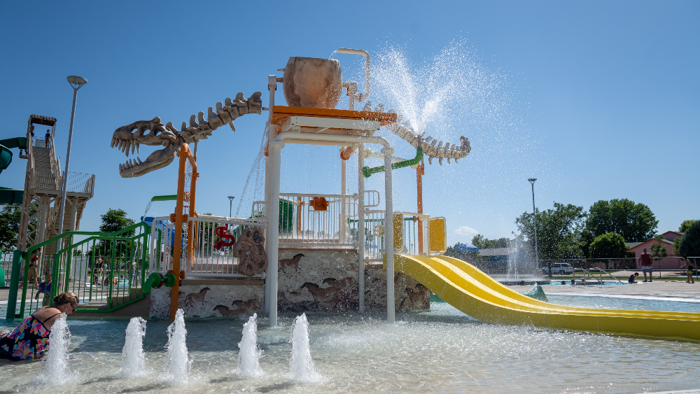 Zero depth pool area at Discovery Bay Waterpark with a dinosaur dump bucket, slide and splash pad.