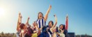 A group of AFLW players banded together and celebrating. One player is in the centre and being lifted up by the group.