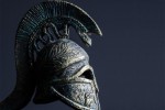 A plumed Greek helmet carved from metal, against a dark blue background