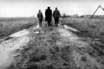 three figures walk away on a muddy road in a stark landscape three figures walk away on a muddy road in a stark landscape